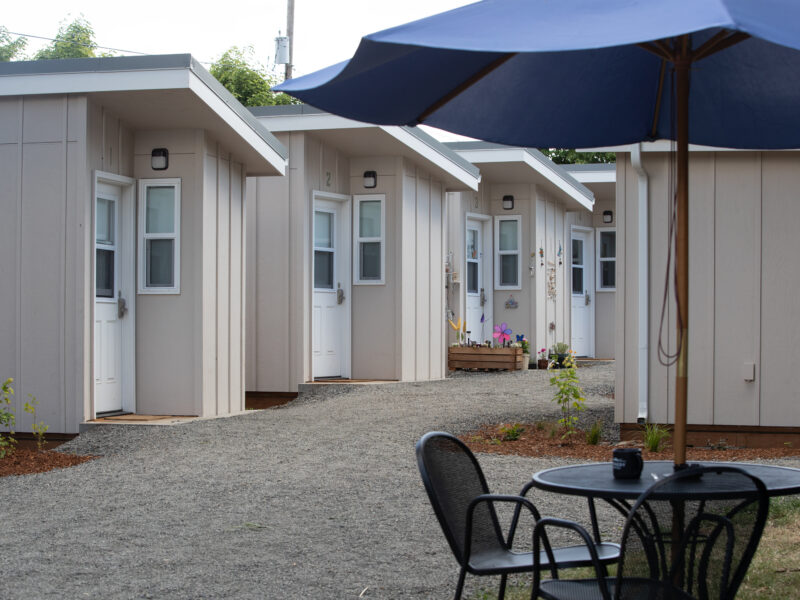 A row of tiny homes on a gravel path, with an umbrella in the foreground.