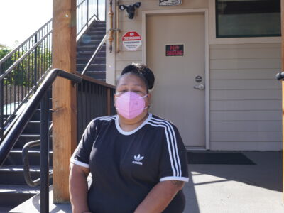 Woman wearing a pink face mask sits outside a building.
