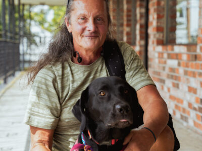 Eric, a FUSE Program participant, kneeling behind his dog, a black Labrador named Misty