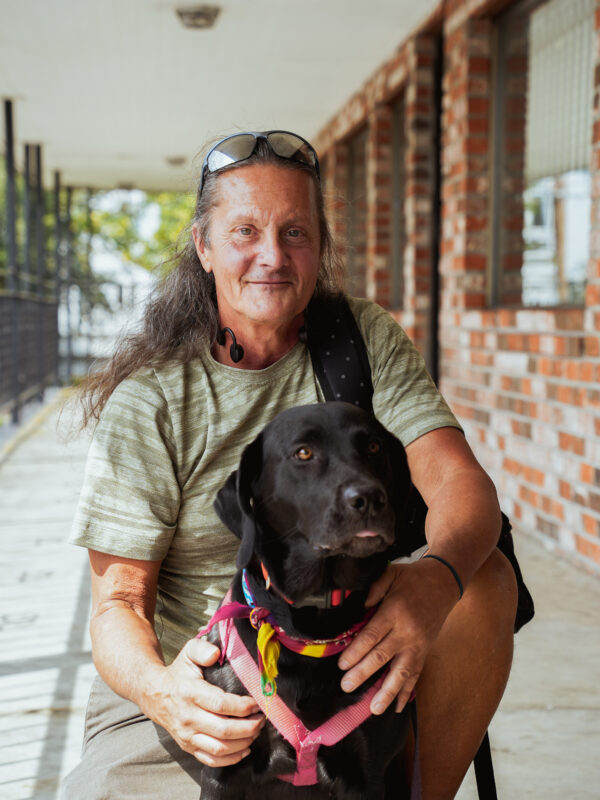 Eric, a FUSE Program participant, kneeling behind his dog, a black Labrador named Misty