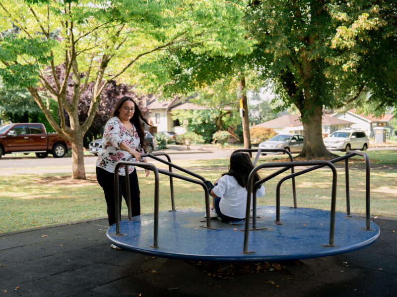 Monique spins her daughter on a merry-go-round in a park.