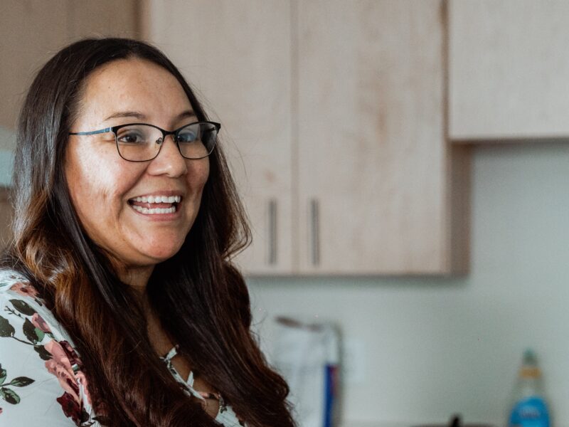 A woman smiles as she stands in her kitchen.