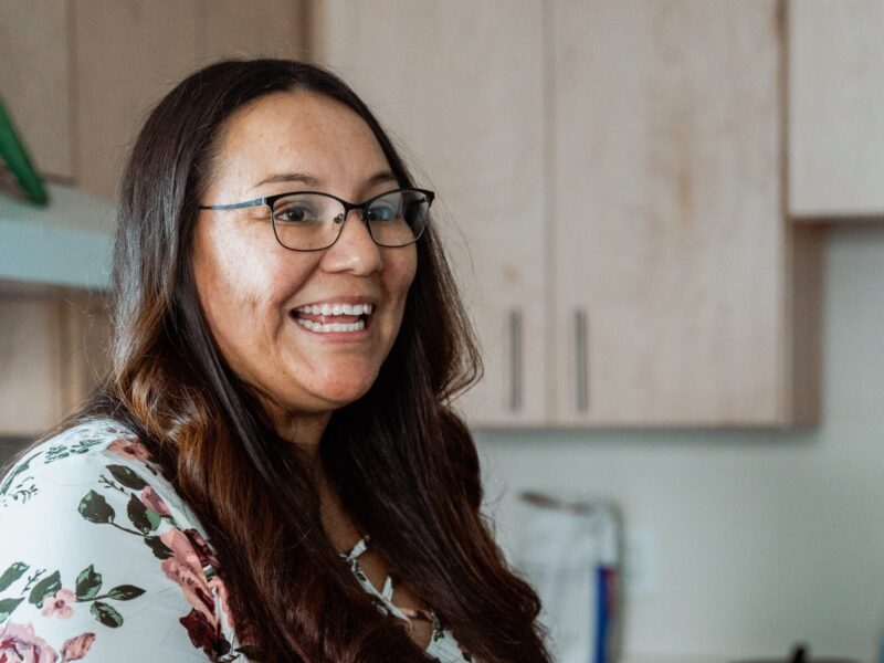 A woman smiles as she stands in her kitchen.