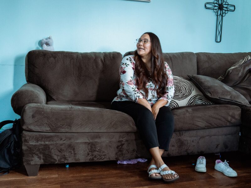 Monique sits on a brown couch and smiles.