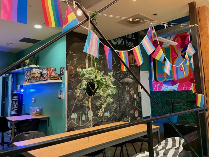 Pride flags hang on a garland over a room with desks and computers.